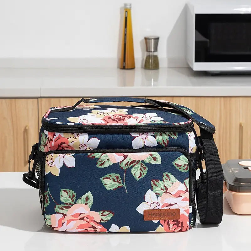Navy blue floral-patterned insulated lunch bag large portable crossbody case with pink and white flowers green leaves black zipper accents and brown leather-like brand patch.
