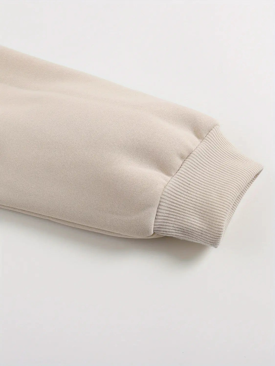 Manga de vellón beige con puños acanalados de la sudadera extragrande crema con estampado peachy, mostrada en un detalle cercano.