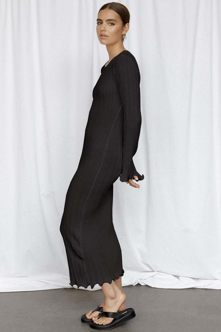 black backless ruffled ribbed knit bodycon maxi dress with long sleeves and a flared hem in soft flowing fabric shown from the back side
