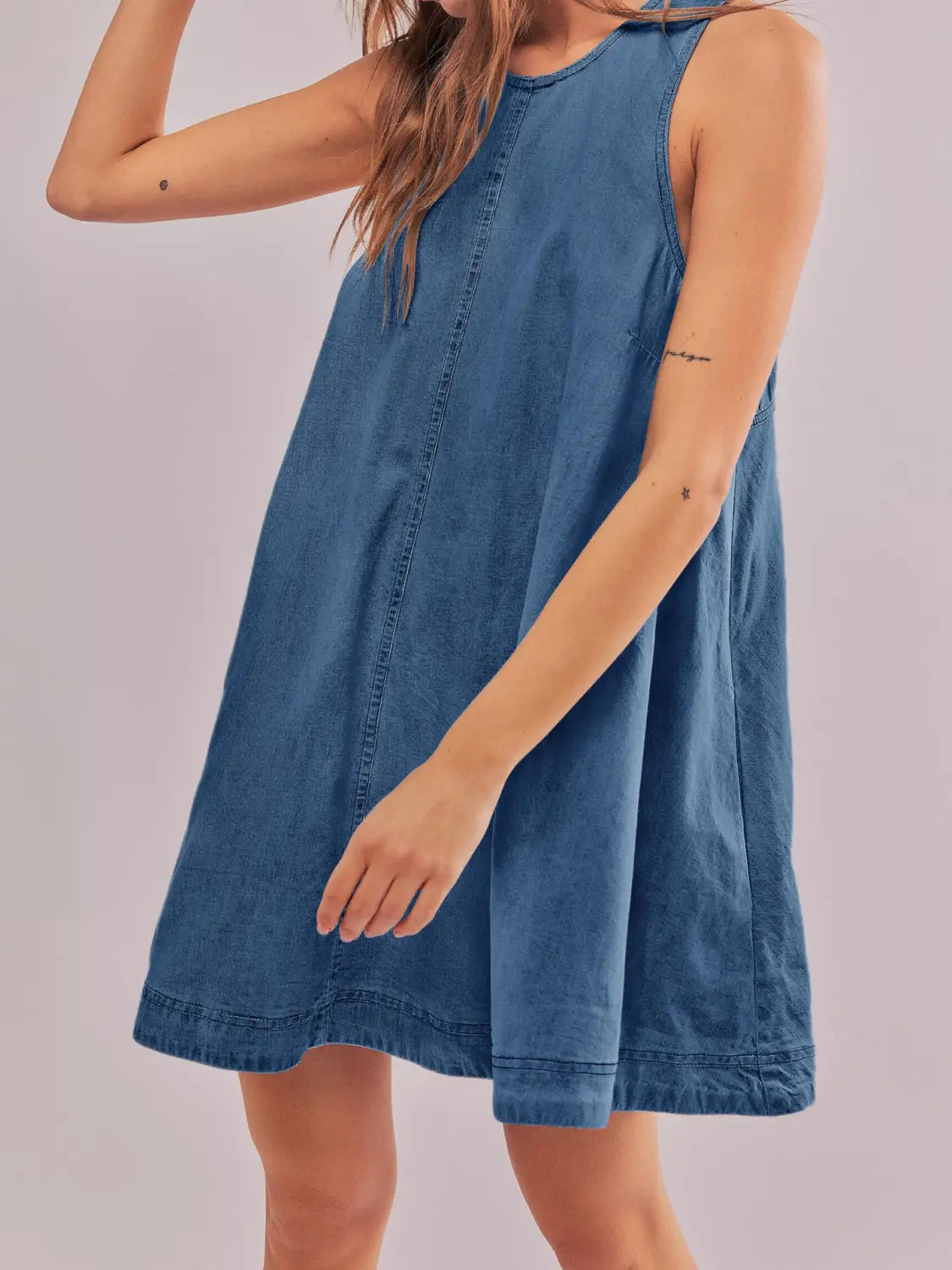 Ein ärmelloses, knie-langes hinten offenes Schleifen-Detail aus Denim-Minikleid in mittlerer Blau-Waschung mit sichtbarer Naht und entspannter Passform