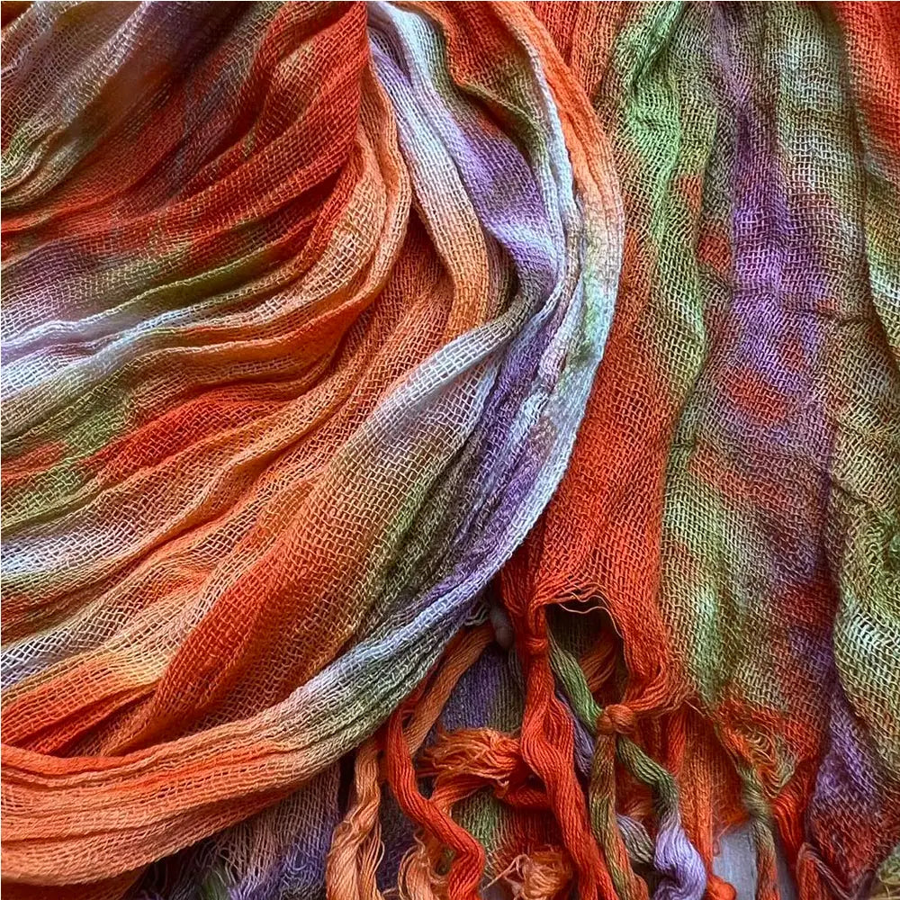 Ein leichter Viskoseschal mit einem kräftigen, locker gewebten Batik-Print mit Farbverlauf aus Orange, Grün, Lila und Weiß.