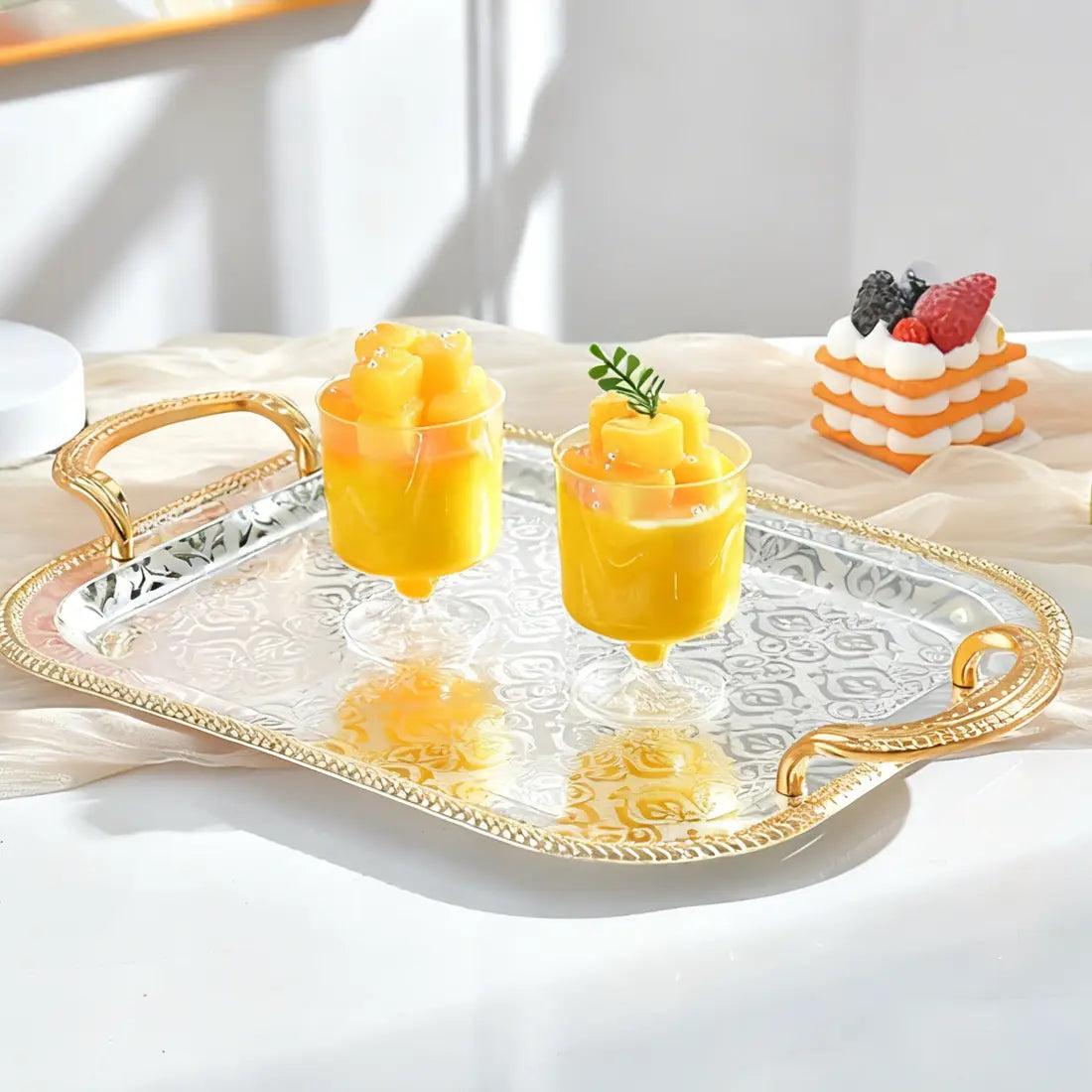 Luxury rectangle serving tray made of silver with gold-toned handles and an ornate embossed pattern.