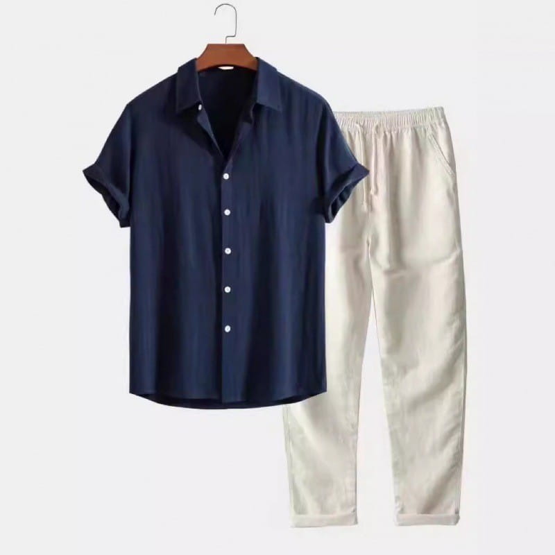Chemise bleue marine pour homme à manches courtes boutonnée, avec des boutons blancs, suspendue sur un cintre en bois, faisant partie d’un ensemble chemise à manches courtes et pantalon.