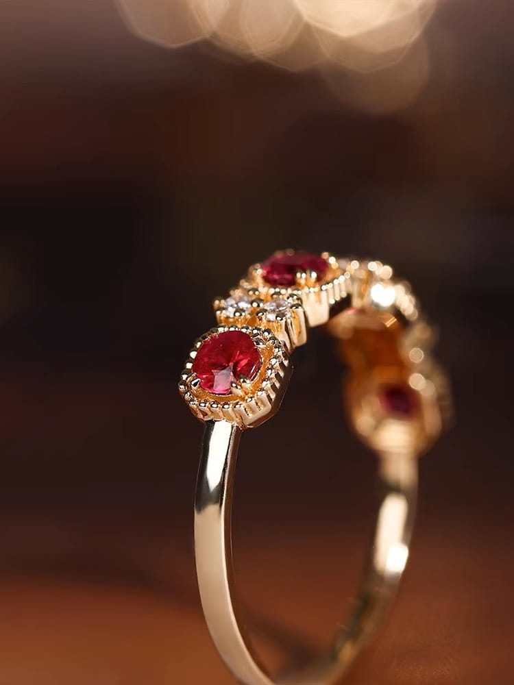 18k gold plated band ring featuring three prominent pigeon blood red rubies set in ornate beaded bezels with smaller clear diamond accents.