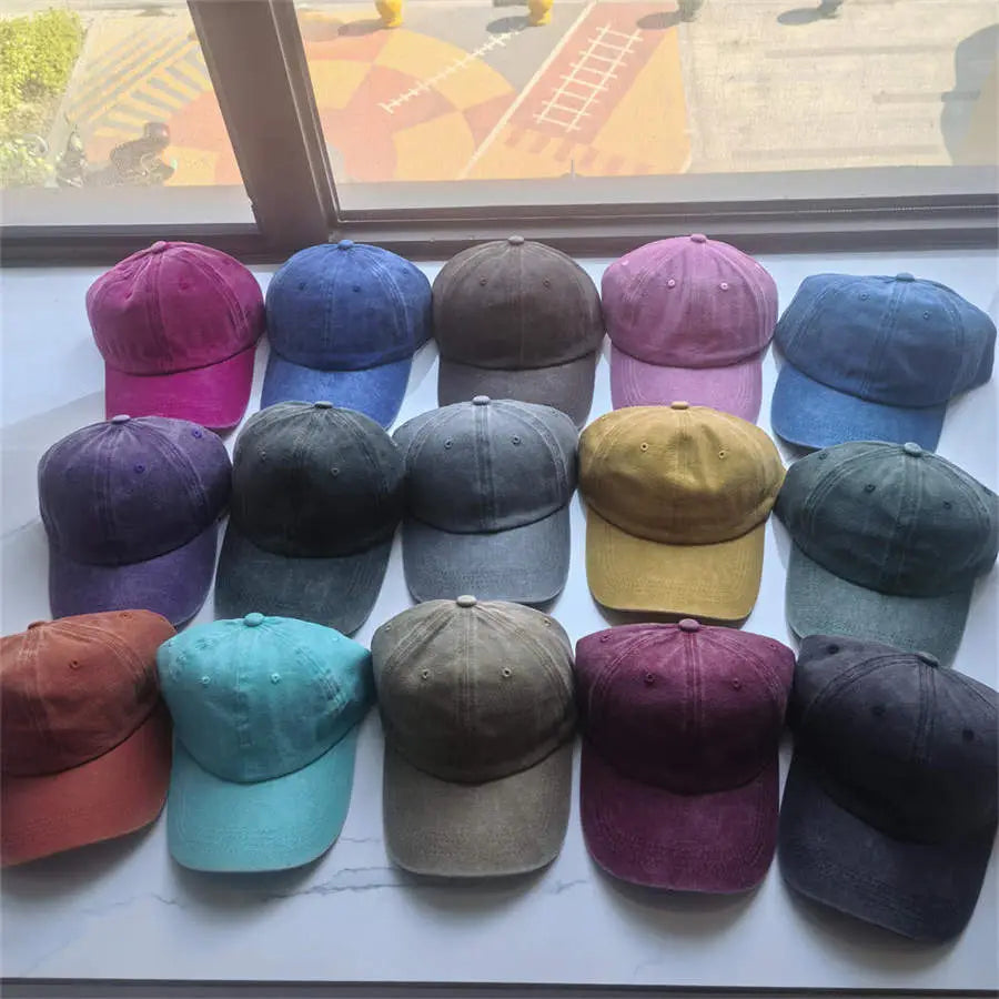 A collection of vintage washed cotton baseball caps in muted and vibrant colors made from soft textured fabric with classic stitched seams.