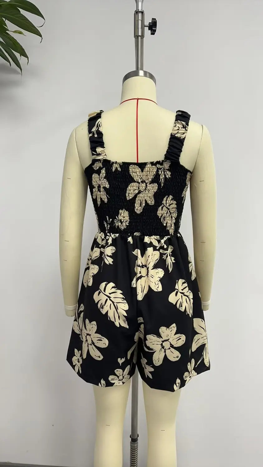 Mono floral negro con flores y hojas en color crema, con tirantes con frunces y cintura fruncida, diseñado como un mono-jumpsuit de playa de verano sin mangas.