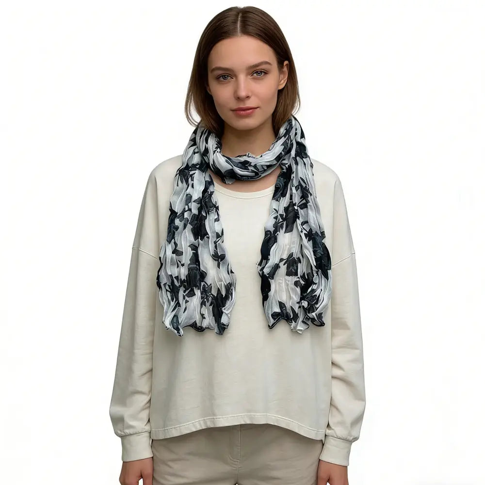 Un foulard en mousseline de crêpe (chiffon) légère et fluide, froissé, orné d’un motif de feuilles florales noir et blanc, porté autour du cou.
