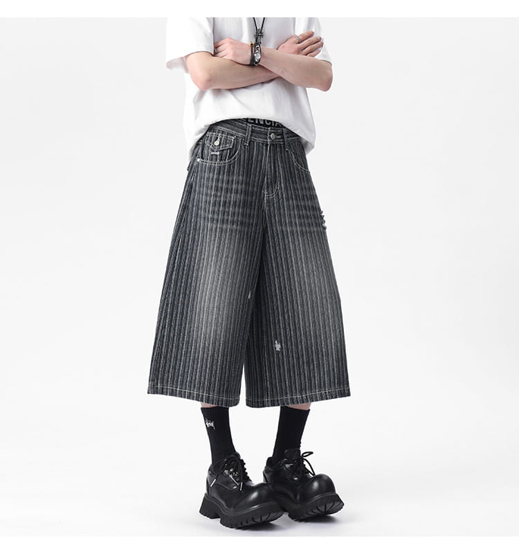 Striped denim capri shorts featuring black and white vertical stripes with a distressed patch on the thigh and a wide-leg design.