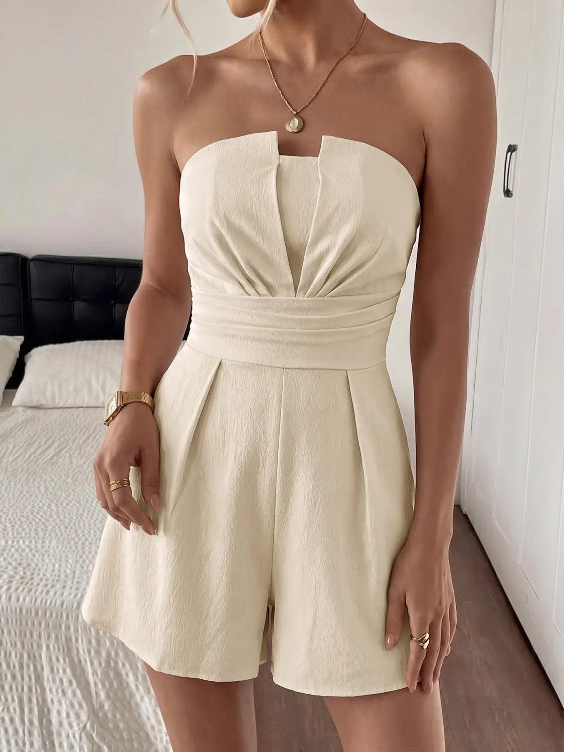 Cream strapless pleated jumpsuit featuring a cream-colored strapless romper with a ruched bodice and pleated shorts.