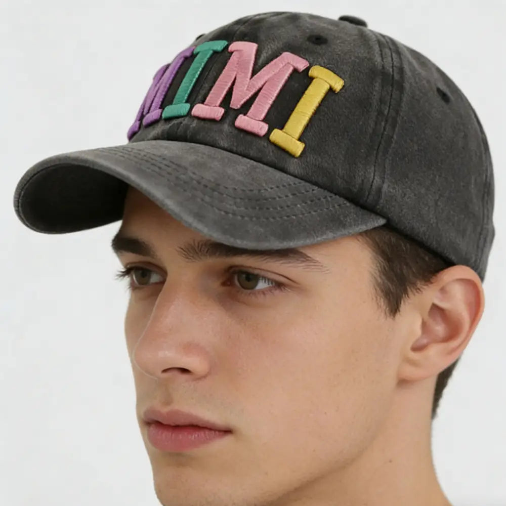 A faded black baseball cap featuring colorful raised embroidery of the word mi from the Rainbow Mimi embroidered baseball cap collection.