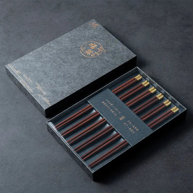 Set aus fünf Paar eleganten dunkelbraunen hölzernen Essstäbchen mit goldfarbenen Spitzen, präsentiert in einer anspruchsvollen schwarzen Geschenkbox.