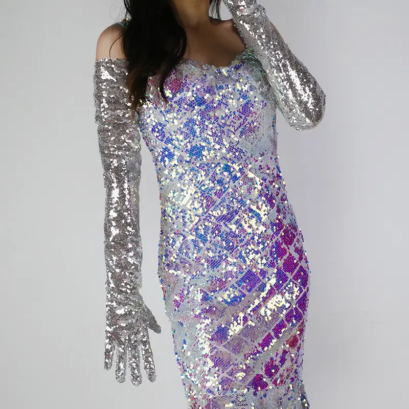 A shimmering iridescent sequined dress with a fitted silhouette and off the shoulder neckline paired with long silver mesh finger gloves.