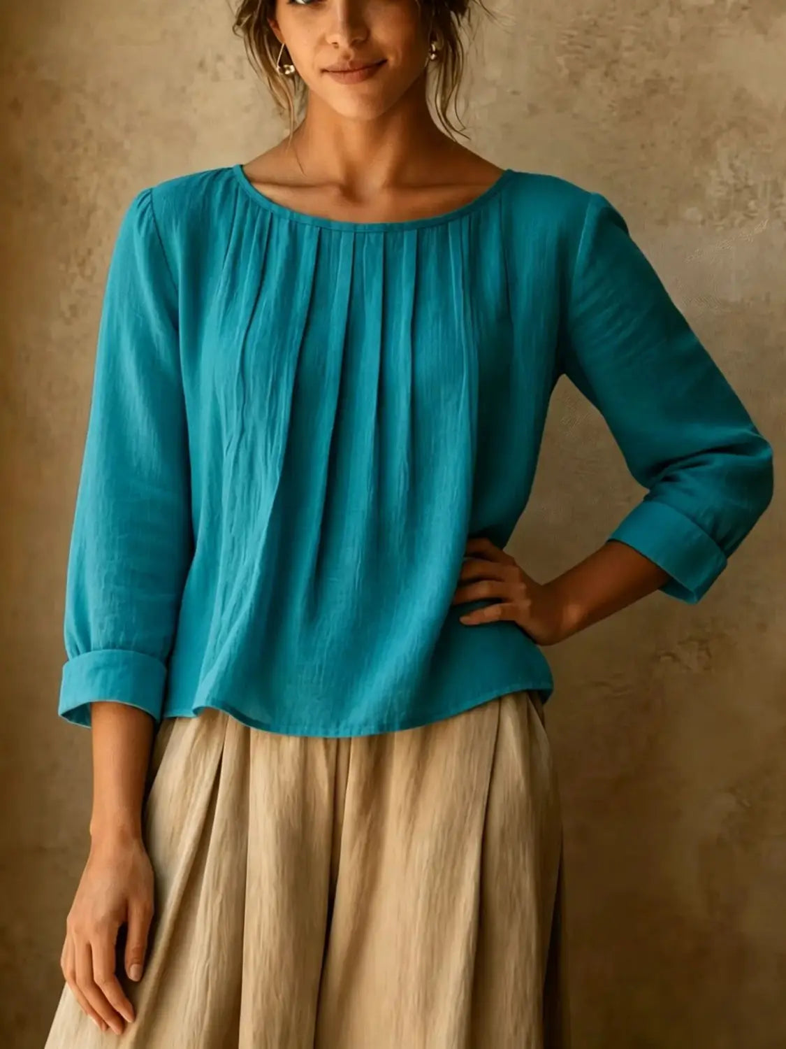 Une blouse ample en lin et coton pour femmes de couleur turquoise, avec encolure froncée et de douces plis sur le buste, dotée de manches trois-quarts.