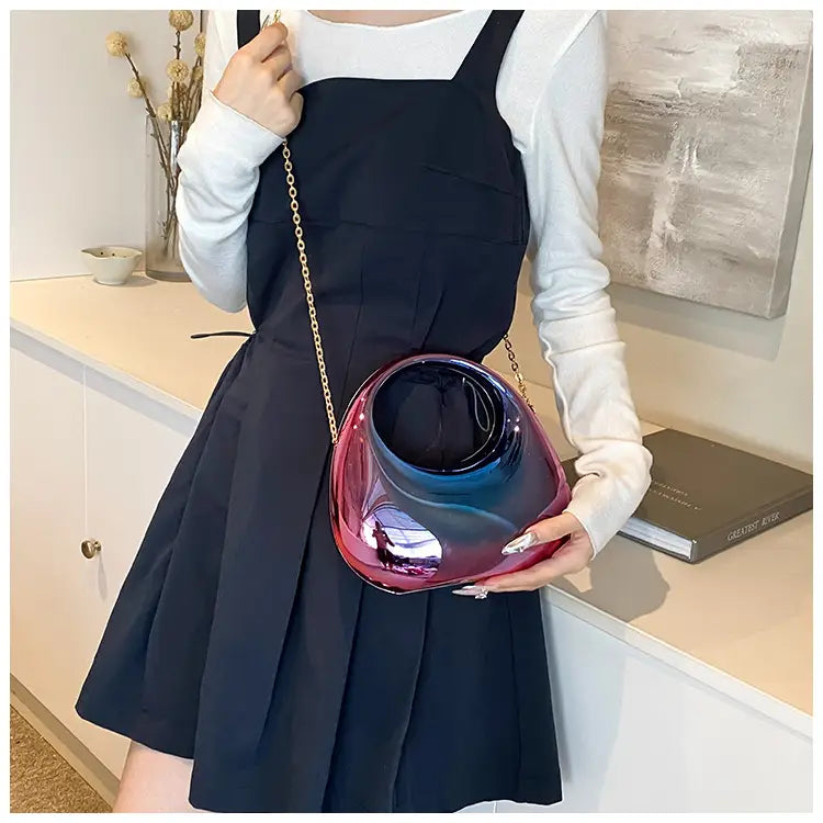 Acrylic gold chain handbag featuring a glossy iridescent glass body with a gradient from deep red to blue hues and a metallic clutch design.