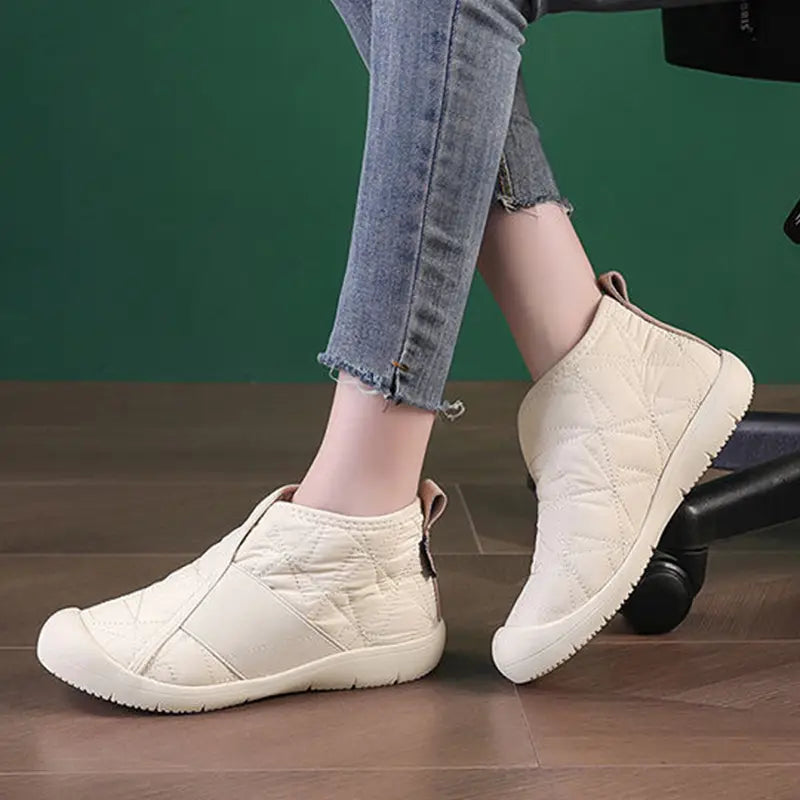Cream-colored waterproof plush winter snow ankle boot with quilted design, brown rubber sole, and elastic side panel.