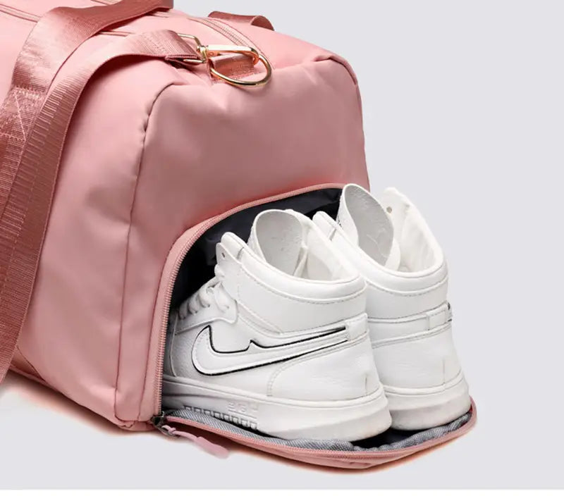 Waterproof oxford pink nylon travel duffel bag with gold tone hardware and a separate shoe compartment holding white Nike sneakers designed for gym and sports.