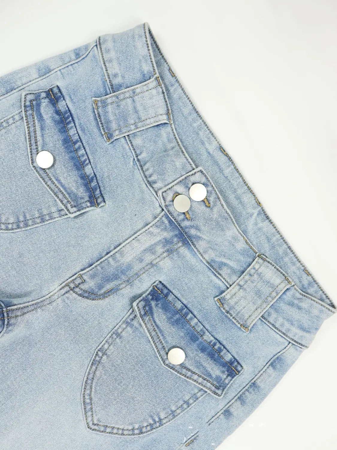 Hell gewaschene Jeansshorts mit mehreren Taschen und silberfarbenen Knopfverschluss-Elementen, passend zu schwarzen Bootcut-Jeans mit hoher Elastizität und schlanker Passform.