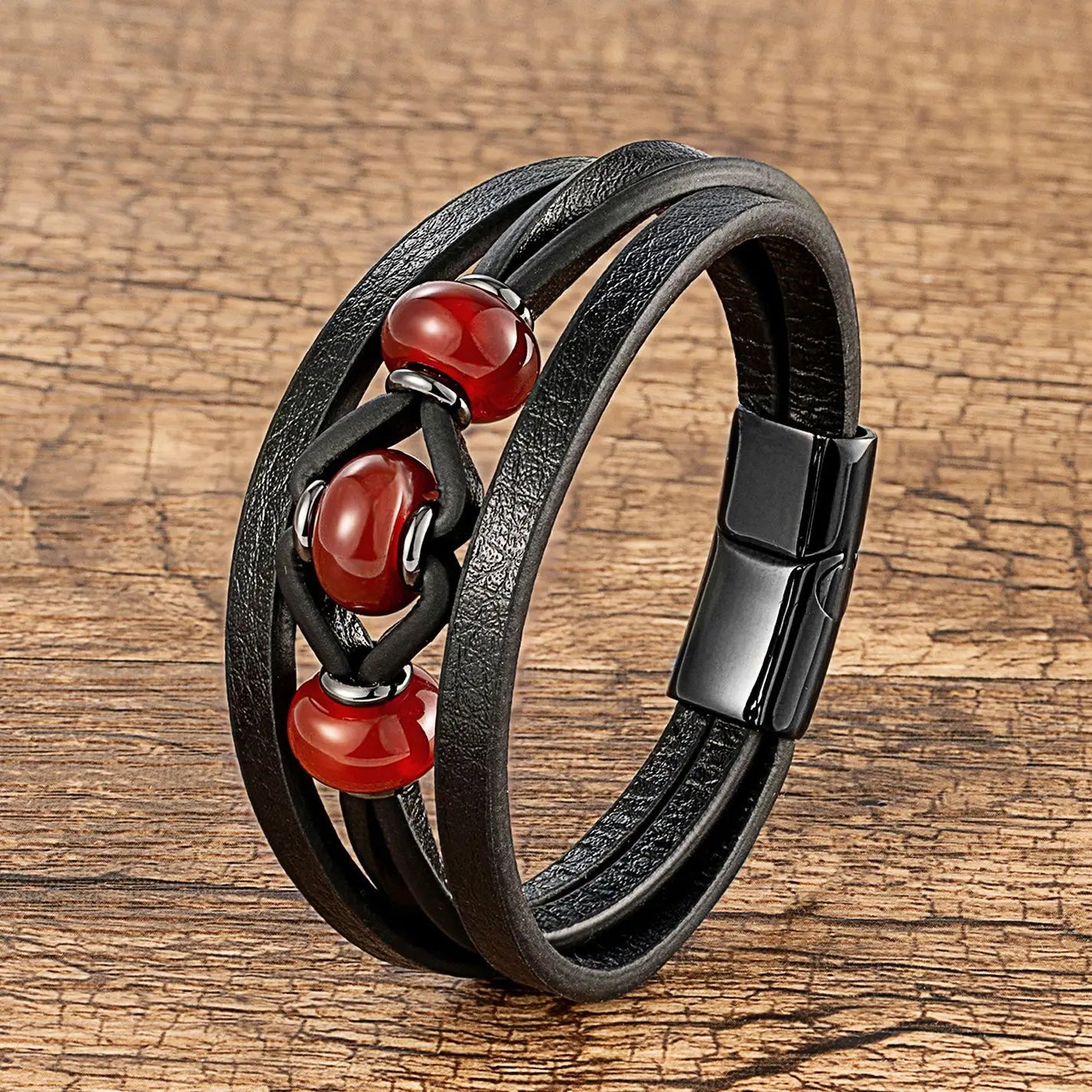 Bracelet en cuir noir à cordons, avec plusieurs brins, comportant trois perles en pierre naturelle rouge lustrée et une fermeture magnétique.