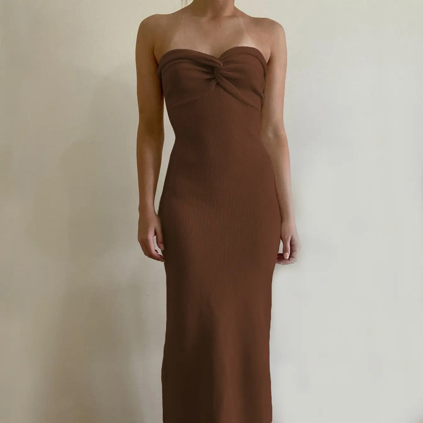 A strapless brown ribbed knit midi dress with a gathered bodice and an off shoulder knotted design.