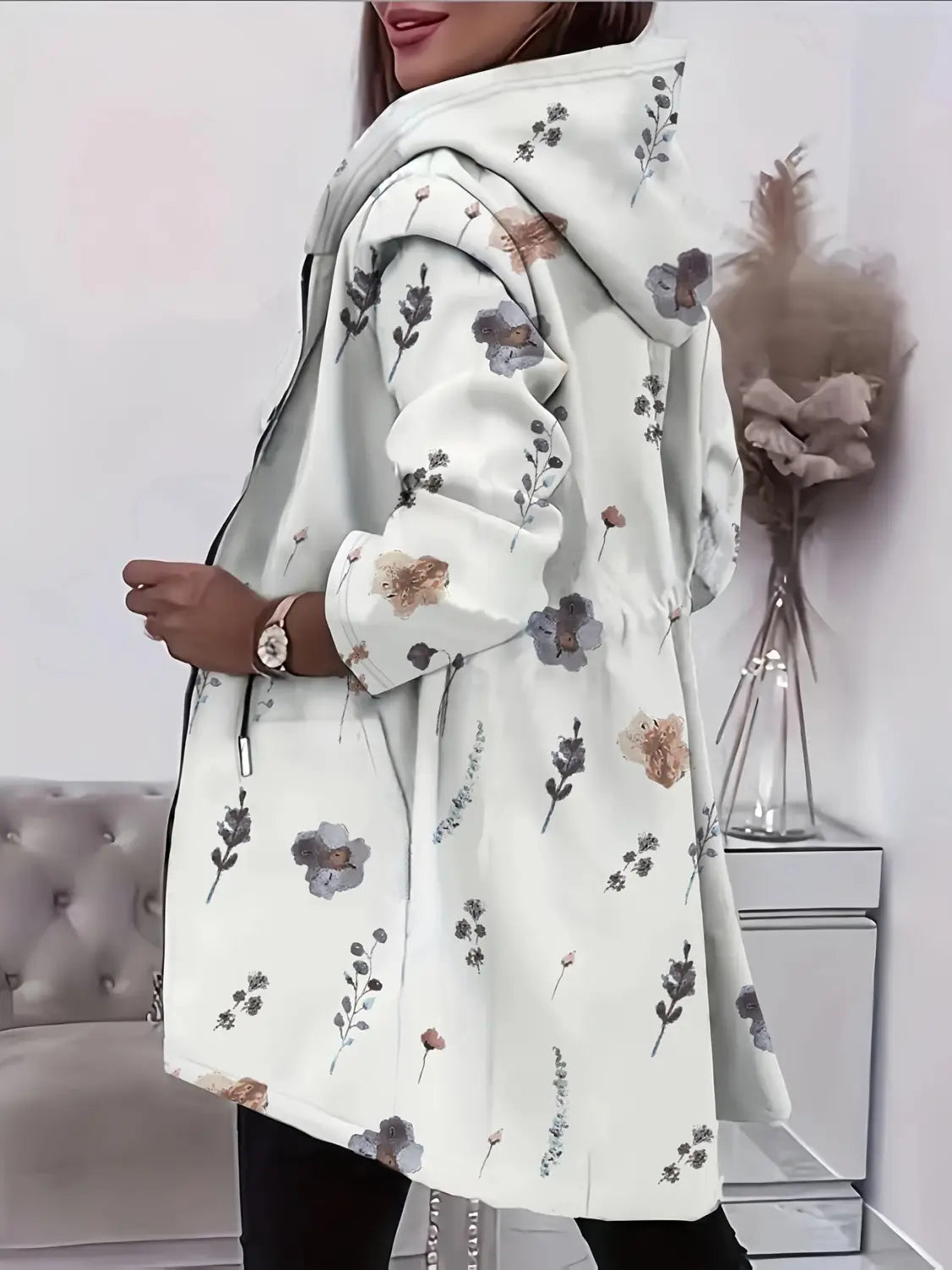 Veste à capuche zippée blanche brodée de fleurs, avec un motif délicat gris et brun atténué, réalisée dans un tissu souple et résistant à l’eau.