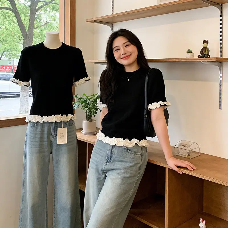 Black short-sleeved knit top with white ruffled trim at the cuffs and hem featuring a colorblock design.