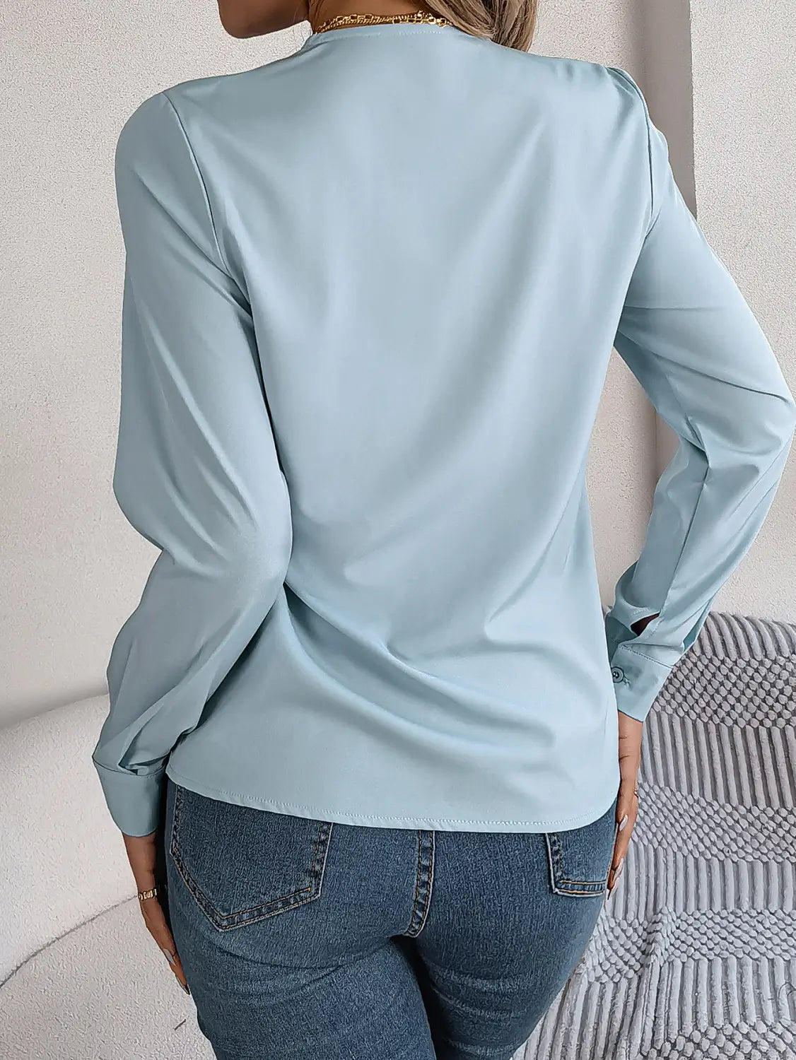 light blue satin long sleeve blouse with sleek fitted back design shown from the back in a white satin v neck wrap blouse with black trim product image