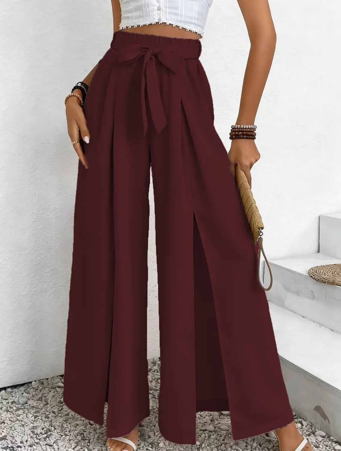 Pantalon ample à taille haute bordeaux, avec une ceinture nouée et une fente avant, conçu comme un pantalon ample et décontracté.