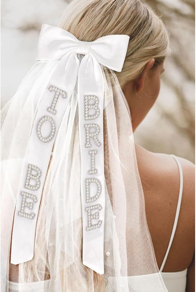 White satin bridal bow veil featuring sparkling rhinestone lettering spelling to be bride tied into a bow at the top.