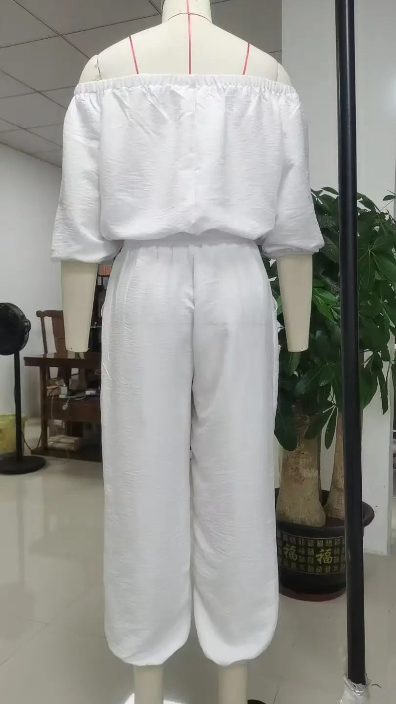 White linen off-shoulder jumpsuit set featuring loose flowing fabric and wide-leg pants.