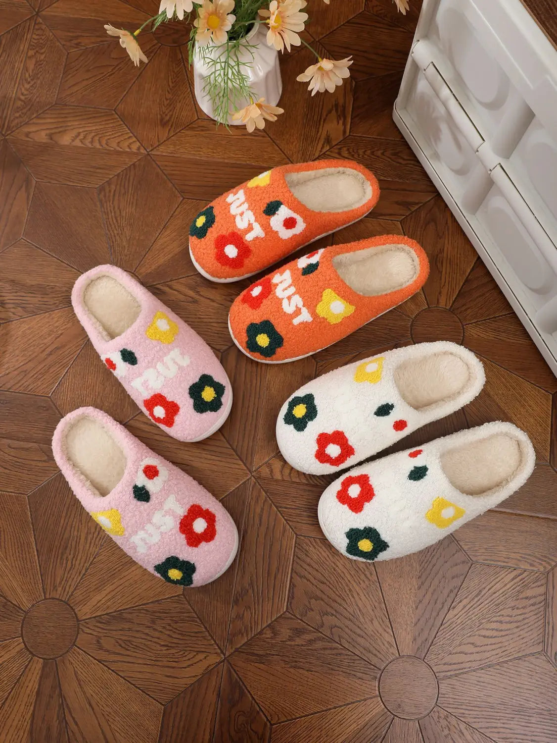 Set of four cozy fuzzy slip-on plush floral cotton slippers in vibrant orange pink and white with soft tpr sole and decorative just text.