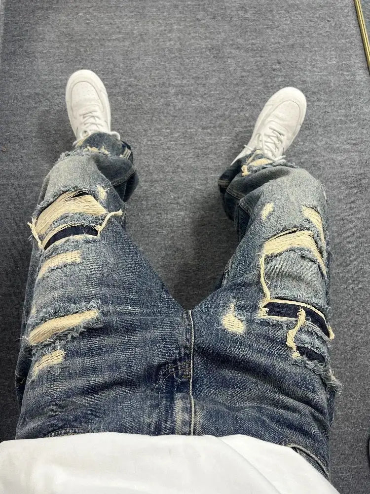 Men’s light blue distressed ripped patch denim jeans made of denim with multiple ripped patches and frayed edges.