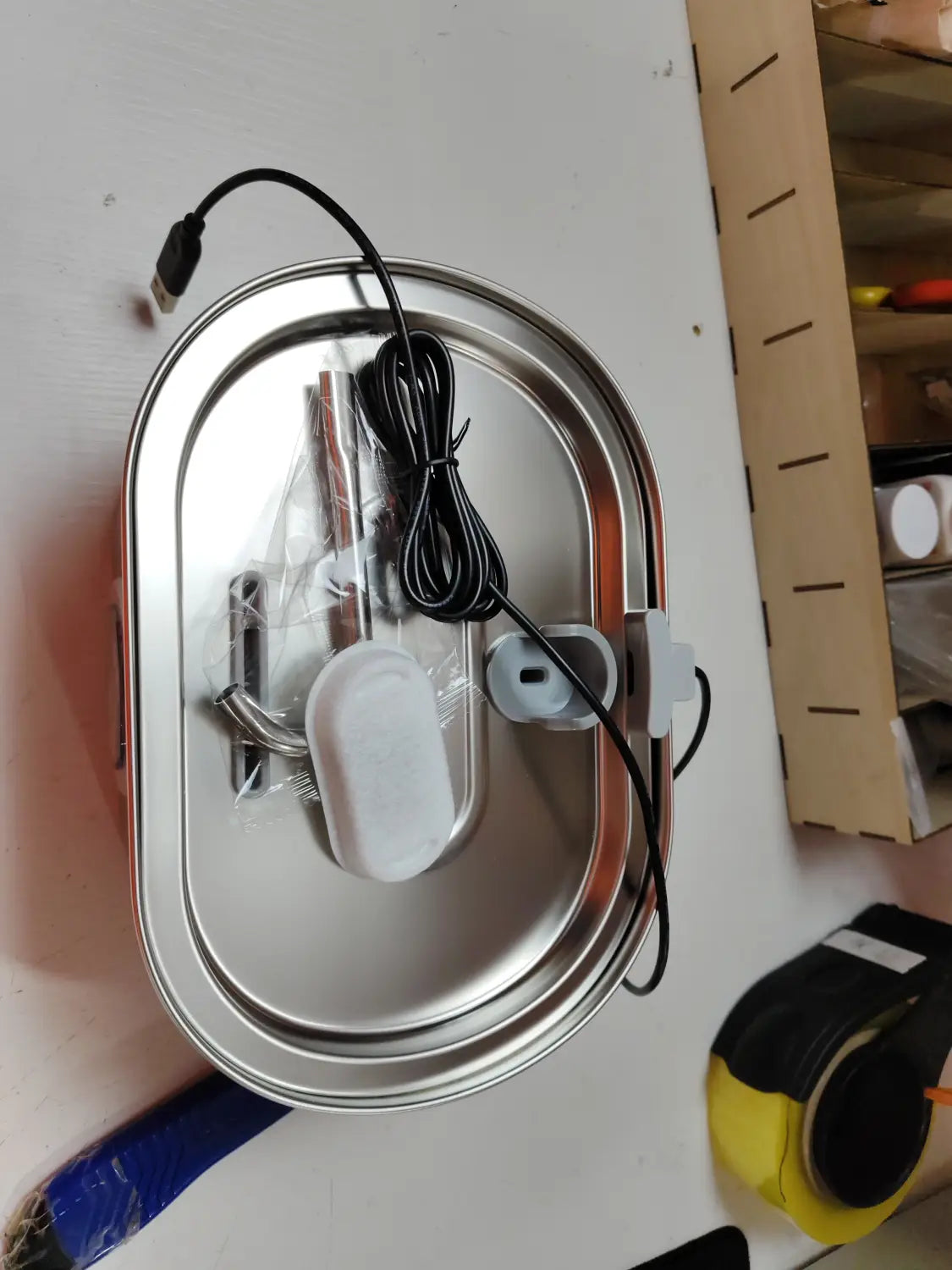 Brunnen für Haustiere aus Edelstahl mit Filter, mit einem oval geformten elektrischen Warmhaltefach im Inneren, weißen Kunststoffkomponenten und USB-Kabel.
