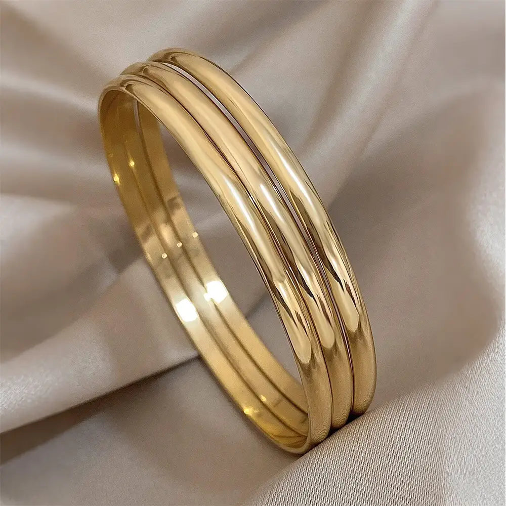 Three sleek gold toned 18k gold plated minimalist stackable bangles with a smooth polished finish.