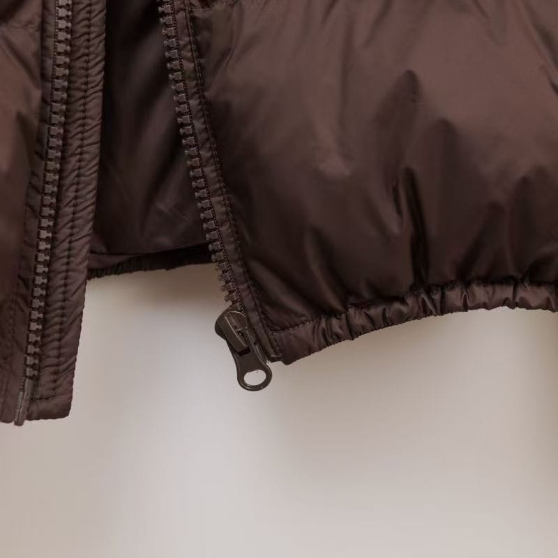 Dunkelbrauner wattierter Steppmantel mit schwarzem Reißverschluss und verschulterten Nähten für warme Winterkleidung.