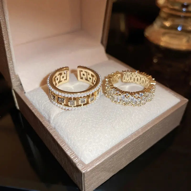 Two gold-toned open hoop rings featuring a hollowed square pearl with embedded square-cut stones and a continuous line of baguette zircon diamonds.