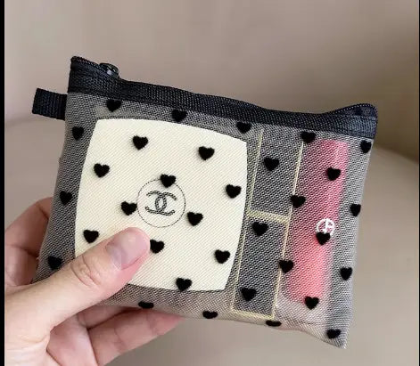 Eine schwarze und weiße, herzgemusterte Mesh-Kosmetiktasche von Chanel mit einem zentralen cremefarbenen Patch mit dem ineinander verschlungenen CC-Logo.