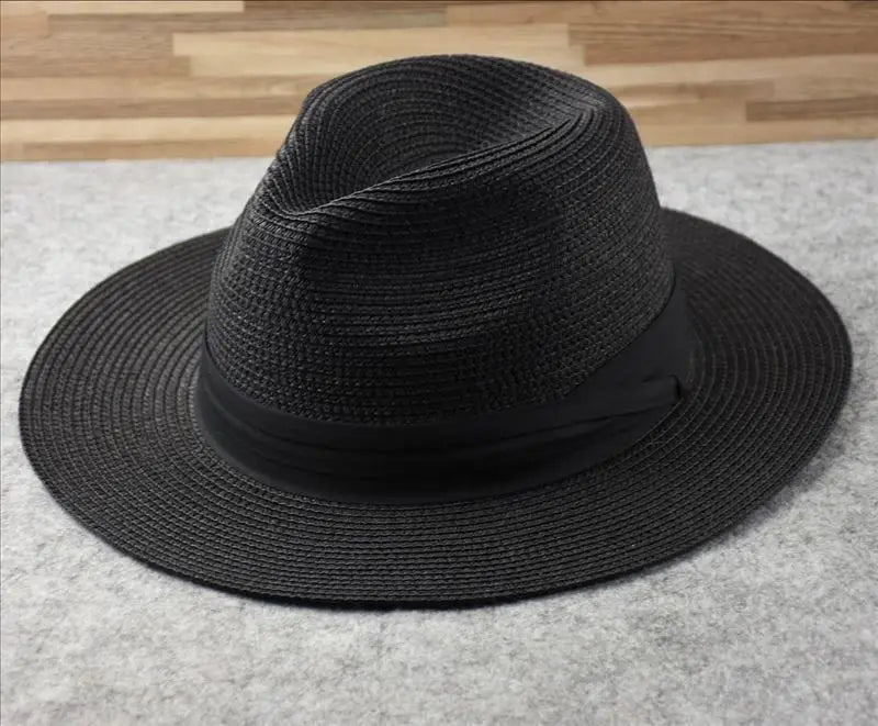 Black woven straw fedora hat with a wide brim and matching black ribbon band designed for foldable sun protection for men.