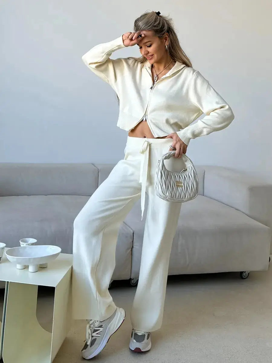 Silver quilted handbag with a structured rounded shape and a small logo paired with a women’s knit zip up cardigan and wide leg pant set.