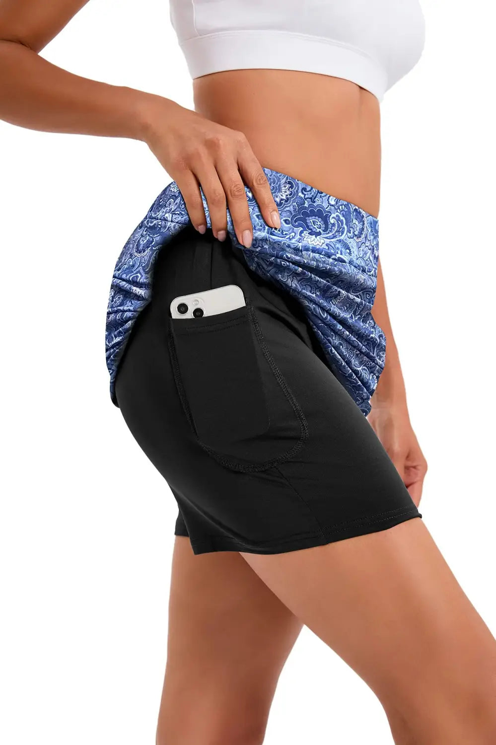 black high-waisted athletic tennis skirt with a blue patterned fabric waistband panel and a side pocket holding a smartphone