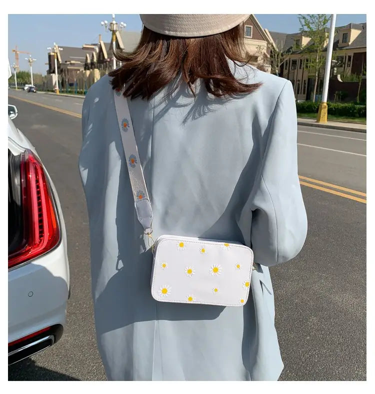 White crossbody bag with yellow daisy embroidery and matching chain strap made of pu leather.