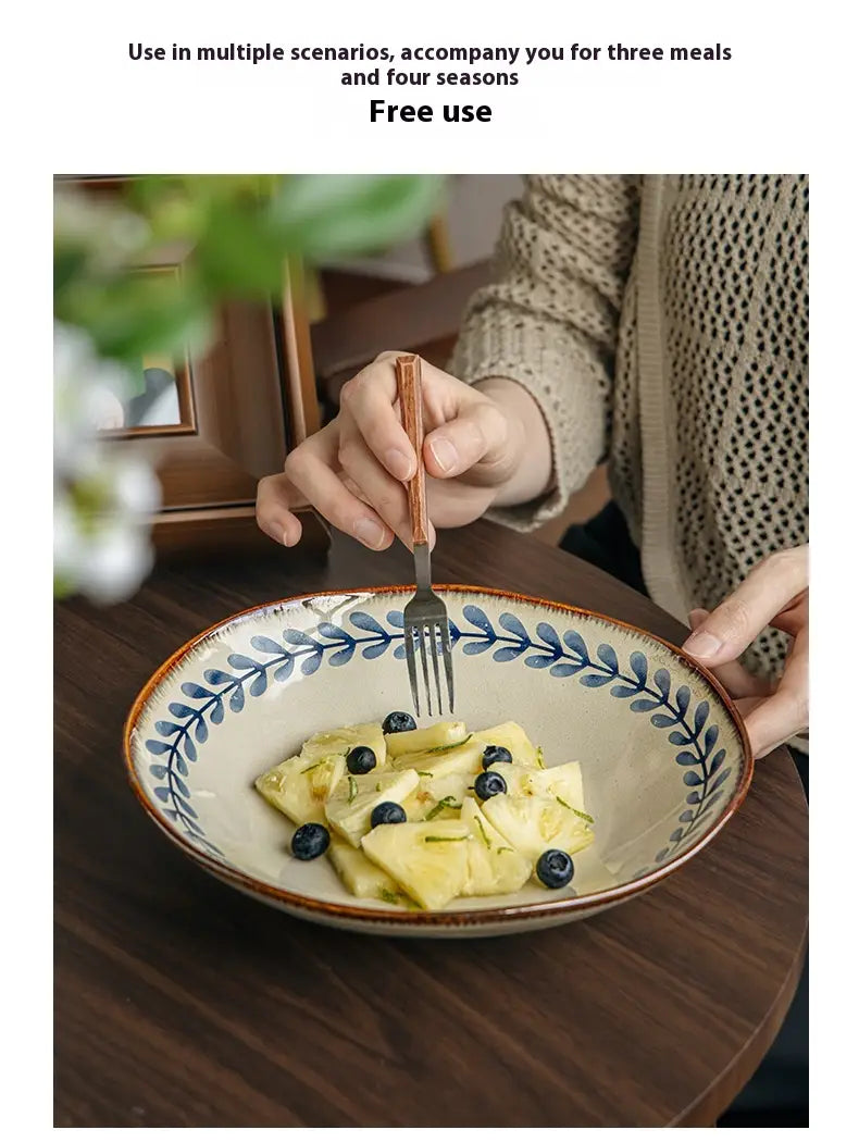 Beige ceramic 9-inch deep plate with blue leaf pattern and brown rim holding sliced fruit and blueberries.