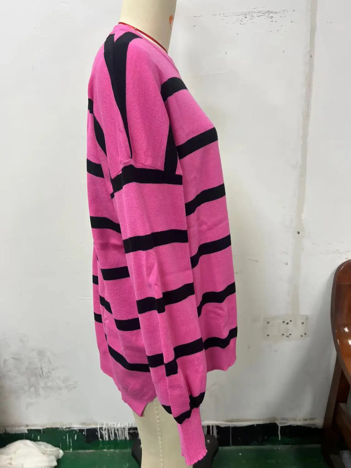 A vibrant pink and black horizontally striped knit cardigan with ribbed cuffs and hem featured as a women’s oversized split color striped knit sweater.