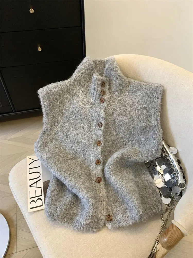 Un cardigan sans manches en maille gris clair à texture douce, avec un col montant et des boutons en bois, conçu comme un gilet tricoté à col haut, boutonné, crème.