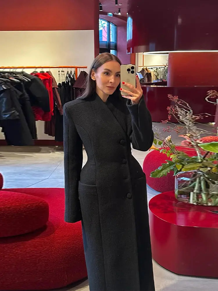 Black double-breasted wool coat with structured shoulders and a high collar designed as waisted long outerwear for women.