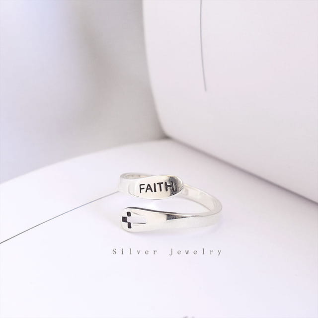 A sleek silver wrap ring with an adjustable band featuring the word faith engraved on one band and a small cross design on the other.