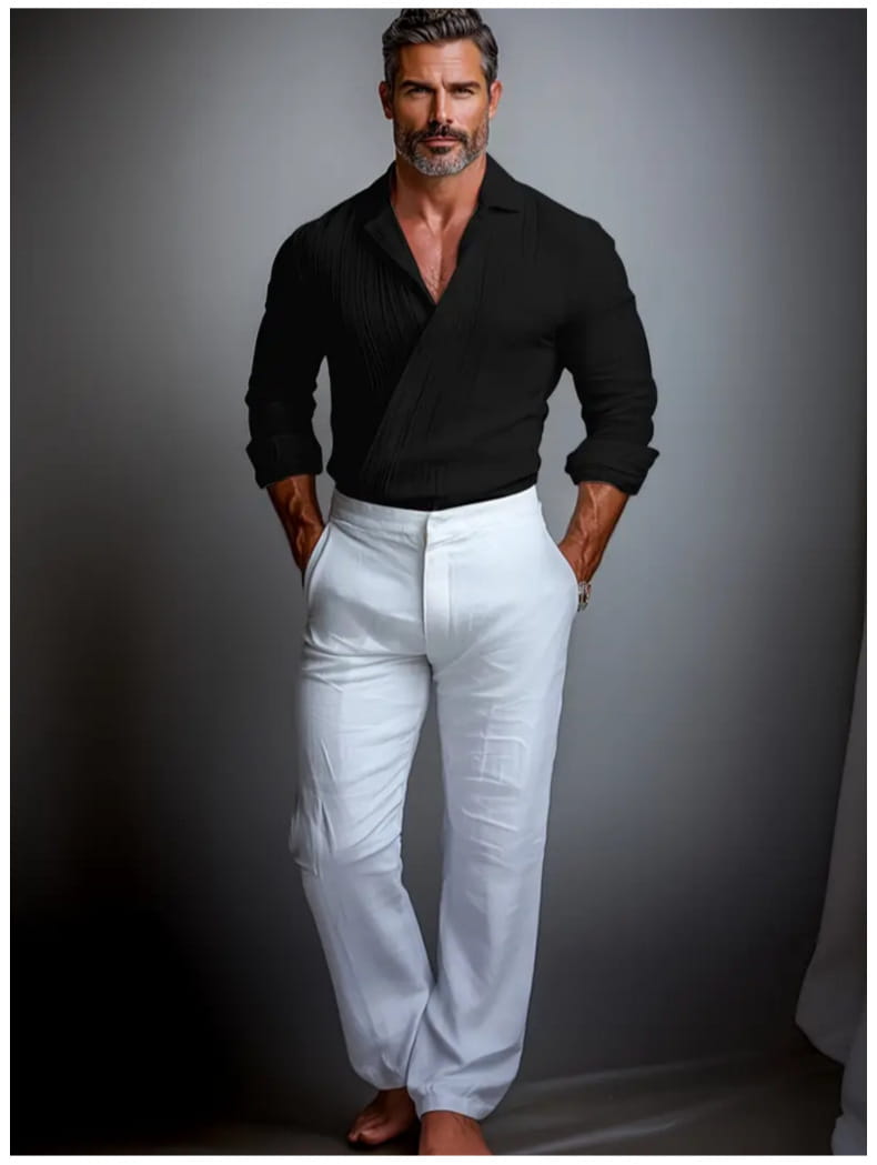 Un homme portant un pull noir à effet portefeuille texturé, manches longues, avec des poignets retroussés, associé à un pantalon blanc
