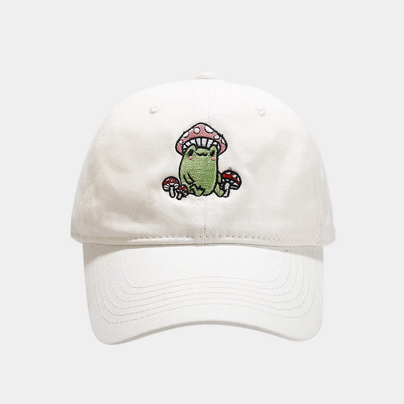 White baseball cap featuring an embroidered design of a green frog surrounded by pink and red mushrooms titled Frog Mushroom Embroidered Baseball Cap.