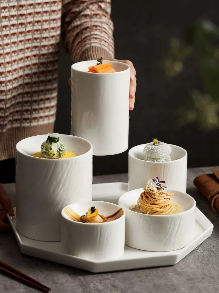 White ceramic cylindrical appetizer bowls with a matte textured finish arranged on an octagonal tray.