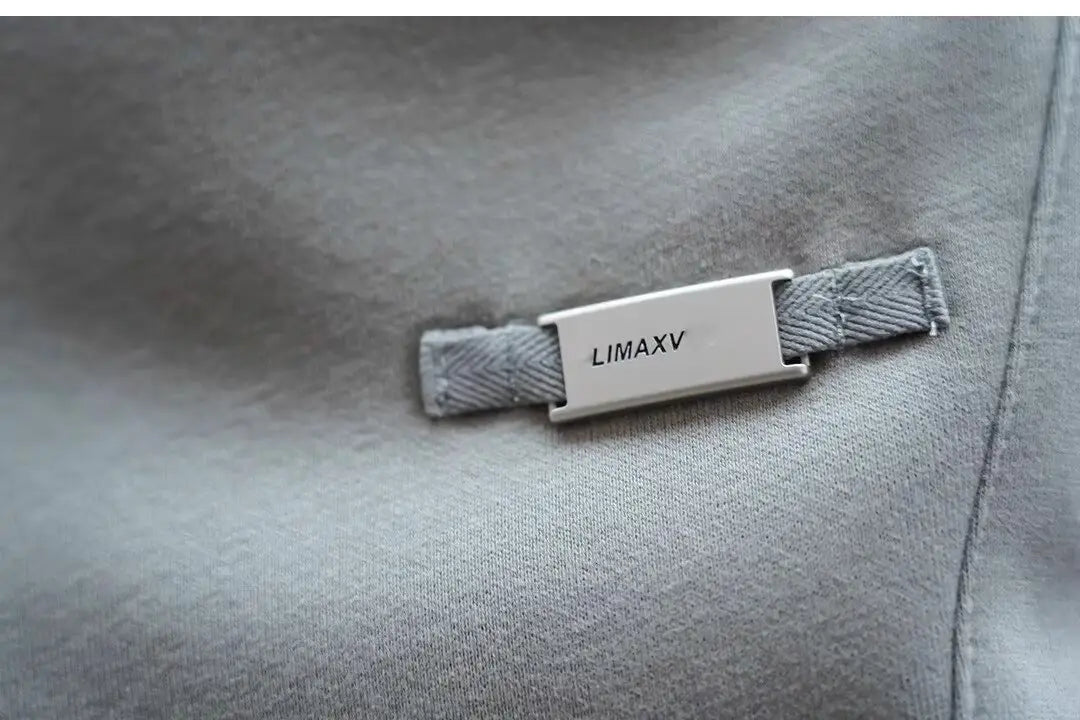 Silver rectangular brand tag engraved with limaxv attached to a gray textured fabric strap on men’s casual solid color sweatpants.