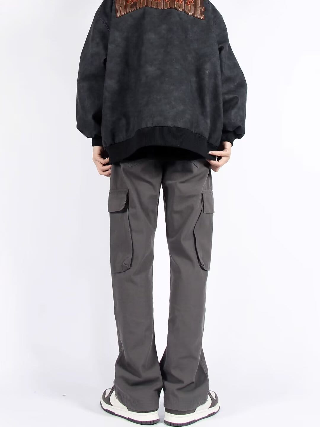 Chaqueta bomber negra, vista desde la parte trasera, con textura desgastada y descolorida y letrero naranja intenso, combinada con pantalones cargo rectos de pierna recta con múltiples bolsillos.